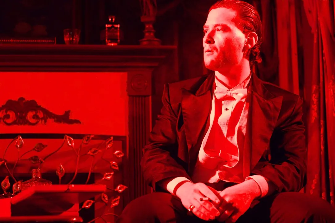 Nimrod Endvelt as Arthur Birling seated under red stage lighting